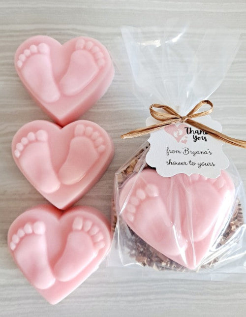 Pink heart-shaped footprints soaps with a gift bag and tag on a light background