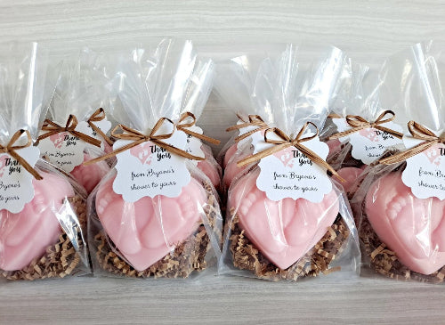 Pink heart-shaped treats in clear bags with brown ribbons and labels on a light gray background