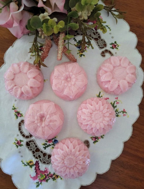 Pink floral soap bars on a decorative white plate with floral patterns.