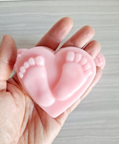 Pink heart-shaped mold with footprints held in a hand against a neutral background