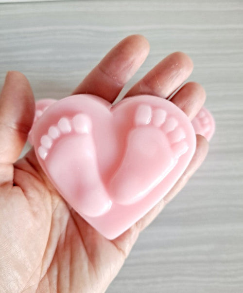 Pink heart-shaped mold with footprints held in a hand against a neutral background